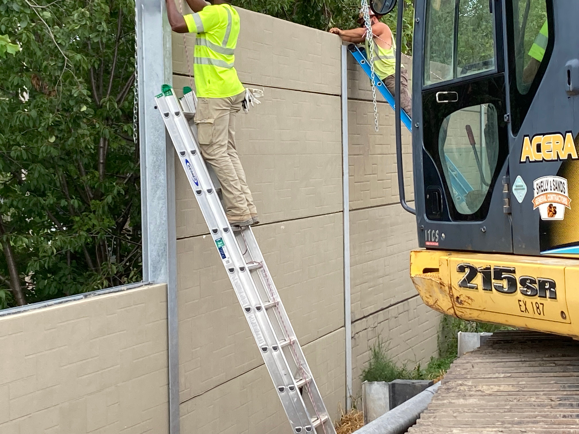 Crew installing a tan brick-pattern Infinity Wall panel between galvanized steel posts